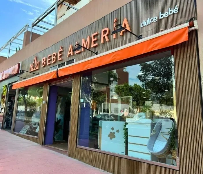 Fachada exterior de la tienda Dulce Bebé Almería con grandes escaparates, mobiliario infantil a la vista y un cartel luminoso en tonos naranja sobre madera.